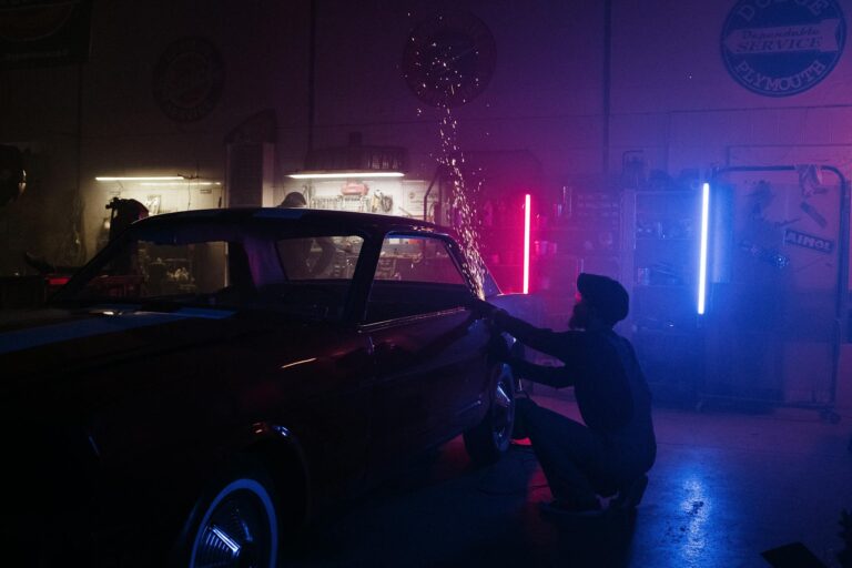 Man in Black Jacket and Black Pants Standing Beside Black Car during Nighttime